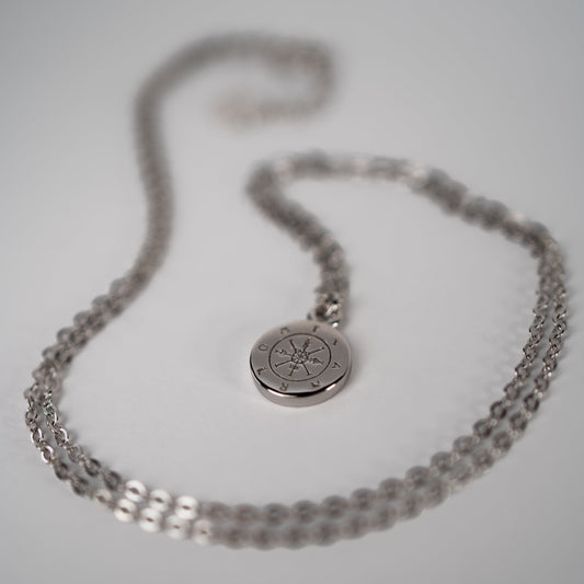 Lula Sea Jewellery journey pendant necklace, sterling silver, necklace features a tiny silver compass hanging from a delicate gold chain. View of necklace on face surface Lula Sea Jewellery New Zealand 