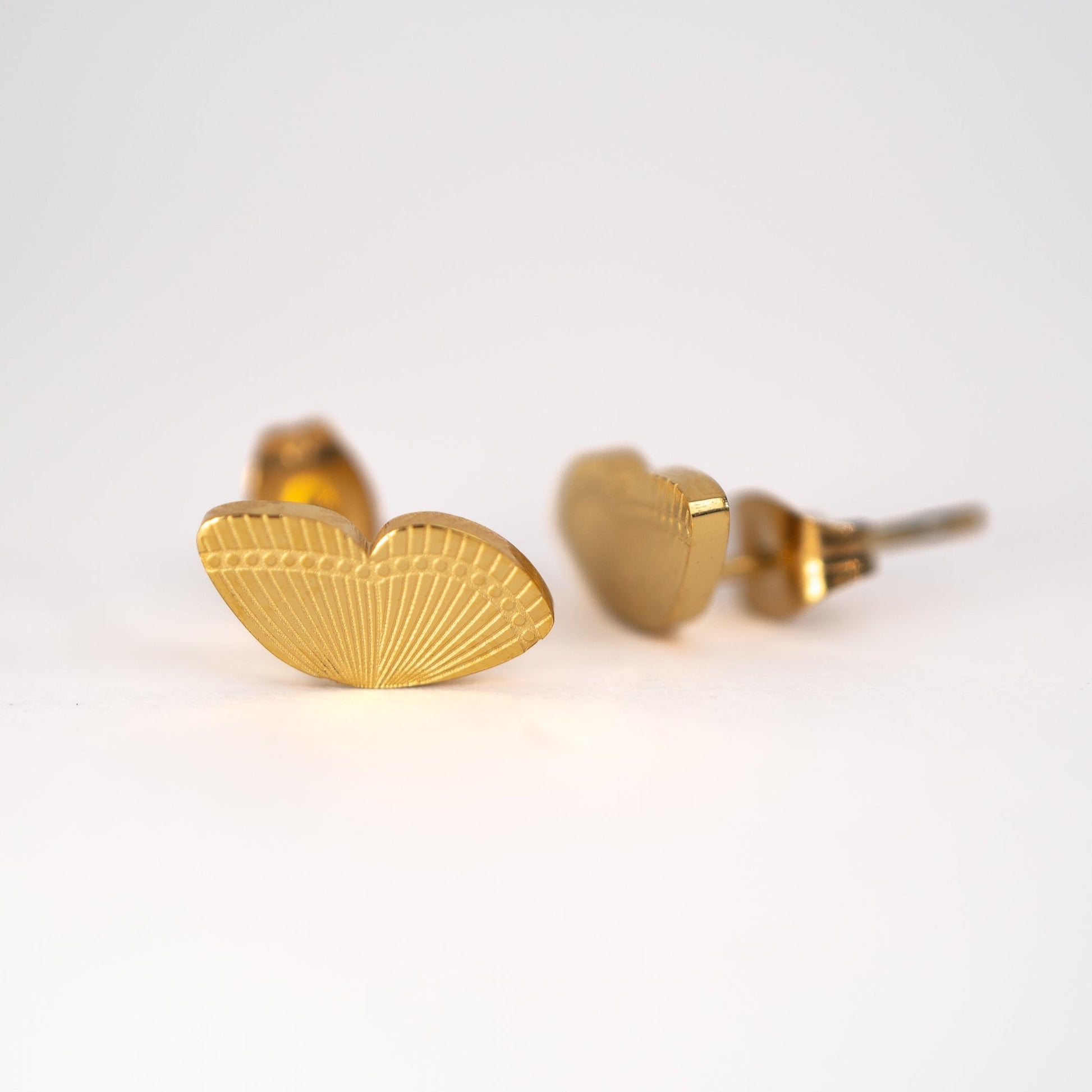 Lula Sea Jewellery, Monarch butterfly wing stud earrings, two single wing stud earrings engraved with the wing pattern gold plated, pictured on flat surface one is turned to the side
